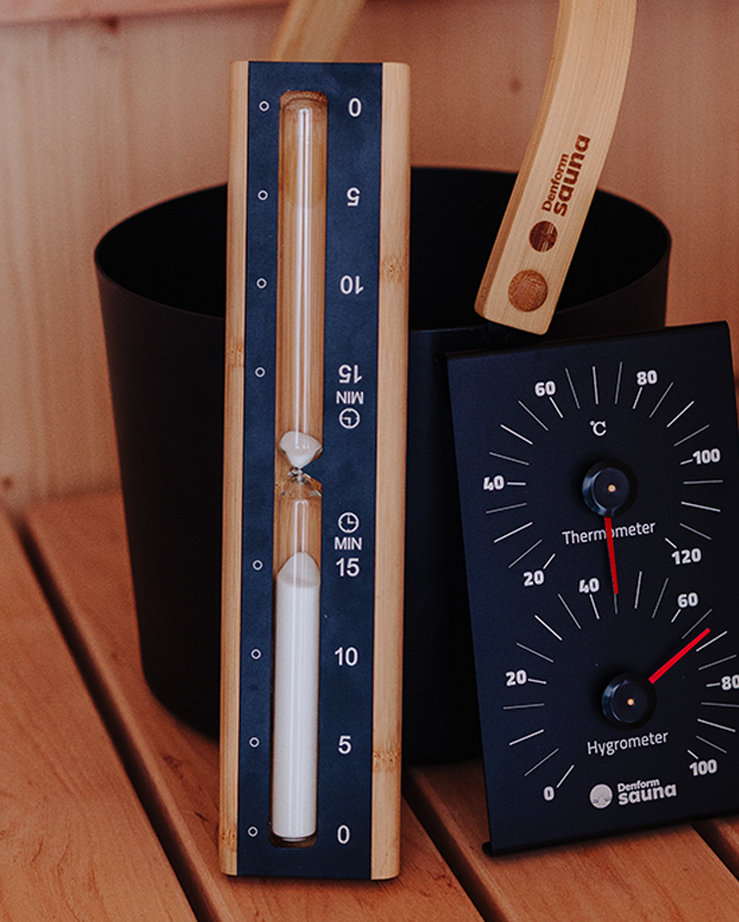 Two sauna thermometers on a wooden surface with a wooden paddle in the background.